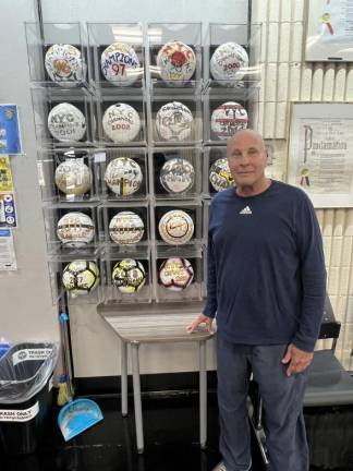 Coach Jake standing nexts to his various championship soccer balls, in the entrance hallway of Amsterdam Avenue’s MLK Jr. High School.