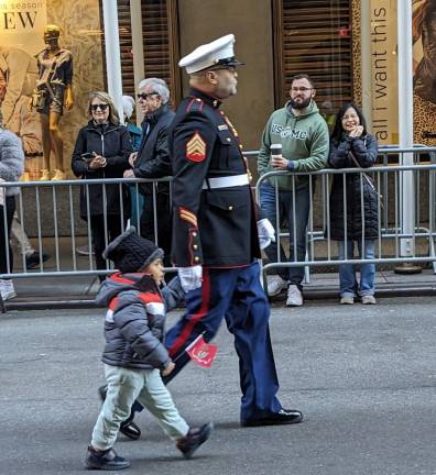 A youngster waves a Siemper Fi flag in the line of march as he is escorted by a veteran USMC sergeant. Photo: Brian Berger