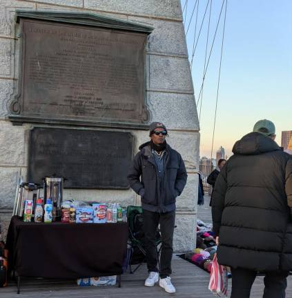 Guarding the Manhattan side of the Brooklyn Bridge is a vendor confidently selling hot cocoa.