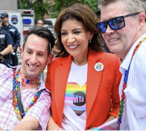 Close up on Governor Hochul—the savior of congestion pricing opponents—and her MTA pride t-shirt, posing with rainbow necklace wearing fans.
