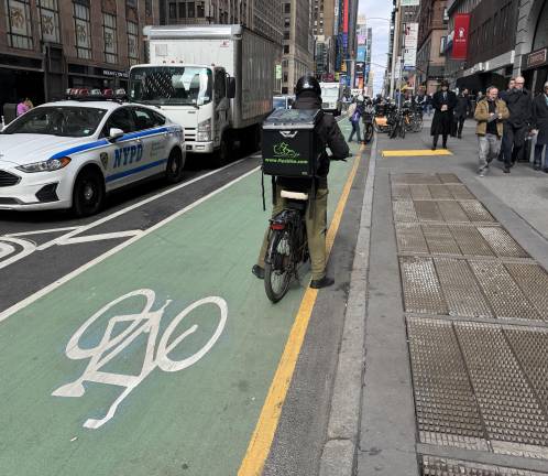 A deliverista stops in the bike lane on 7th Avenue, going the wrong way, before continuing, still heading north in the southbound bike lane, in the direction of 39th Street.