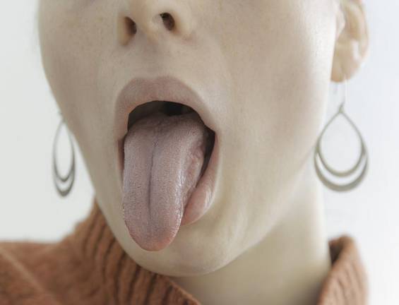 Woman in an orange sweater sticks out her tongue. Scientists note that the tongue is one of the most flexible muscles in the body, able to stretch or shrink, get longer and shorter, go up and down, bend backwards, and round itself into groves.