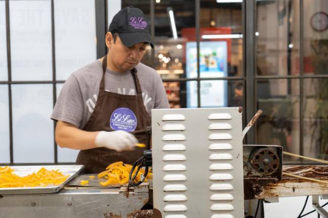 A chocolatier places orange peels into the flat-escalator like surface, to coat them in chocolate.